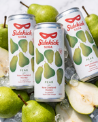 Three chilled Sidekick Pear cans on ice with fresh pears on white marble