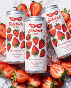 Three chilled Sidekick Strawberry cans on ice with fresh strawberries on white marble