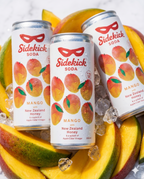 Three chilled Sidekick Mango cans on ice with fresh mango slices on white marble