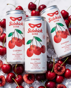 Three chilled Sidekick Cherry cans on ice with fresh cherries on white marble